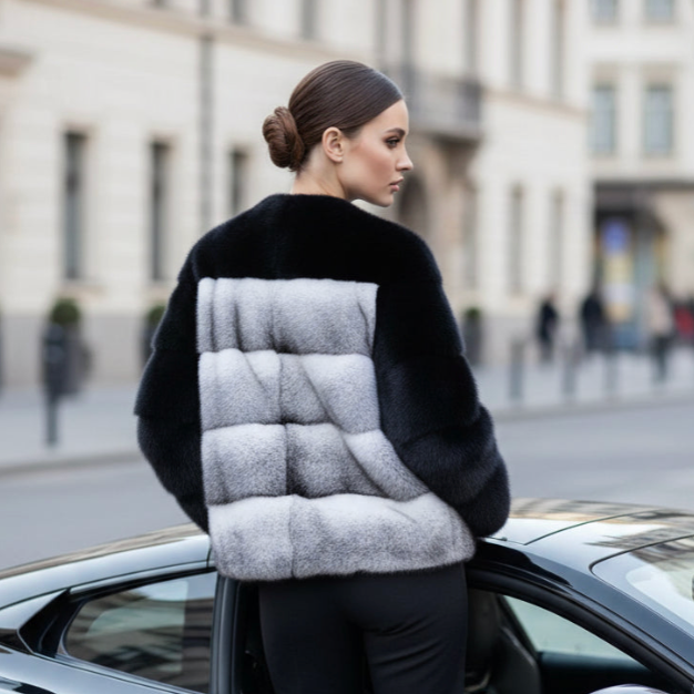 Woman wearing a navy blue jacket with a cross mink colour block back standing next to a car on a city street.