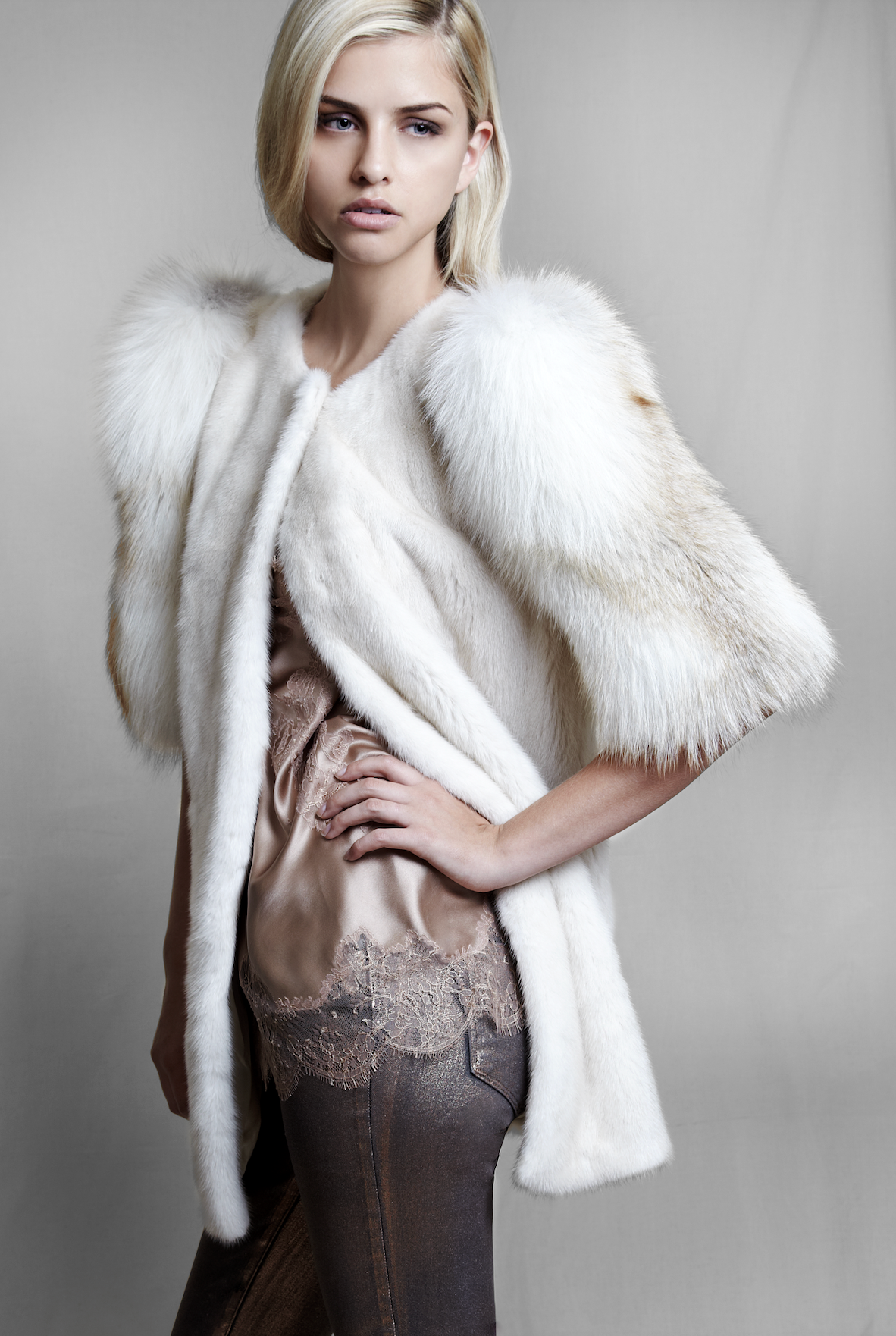 Woman wearing a white fur mink jacket from. lilly e violetta over a lace top and dark skirt on a plain background