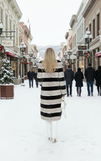 A woman wearing a beige, black, and white striped mink fur coat with a turtle neck and blue jeans.
